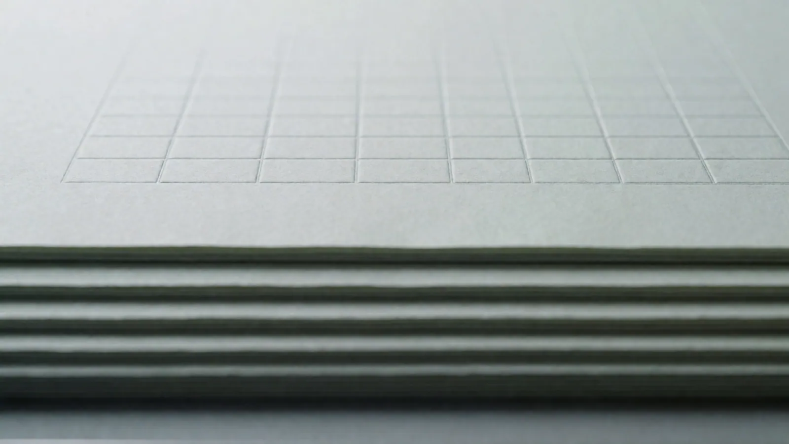 Several blank sheets fanned across a desk in raking light, ruled by shadow rather than by print