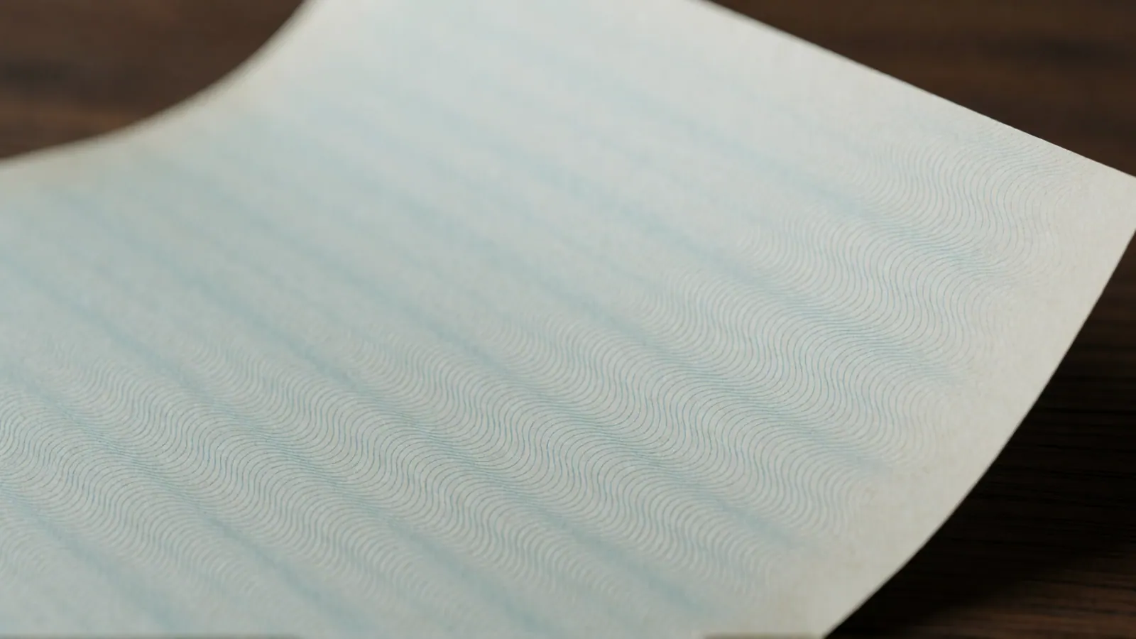 A single blank sheet of cream registry paper lying square on an oak desk under a lamp, nothing printed on it