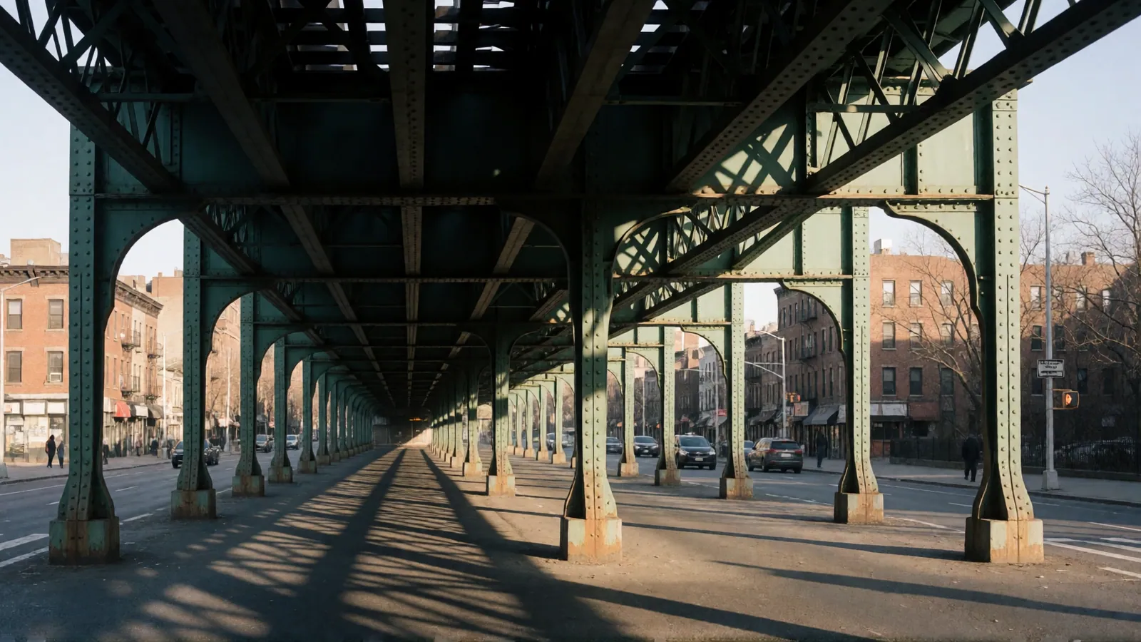 The street under the elevated line on Roosevelt Avenue in flat daylight, the pavement empty
