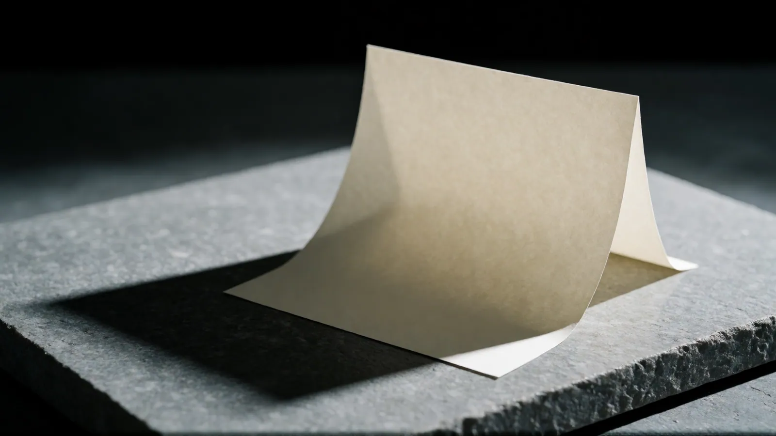 A single blank folded sheet standing on stone under a hard light