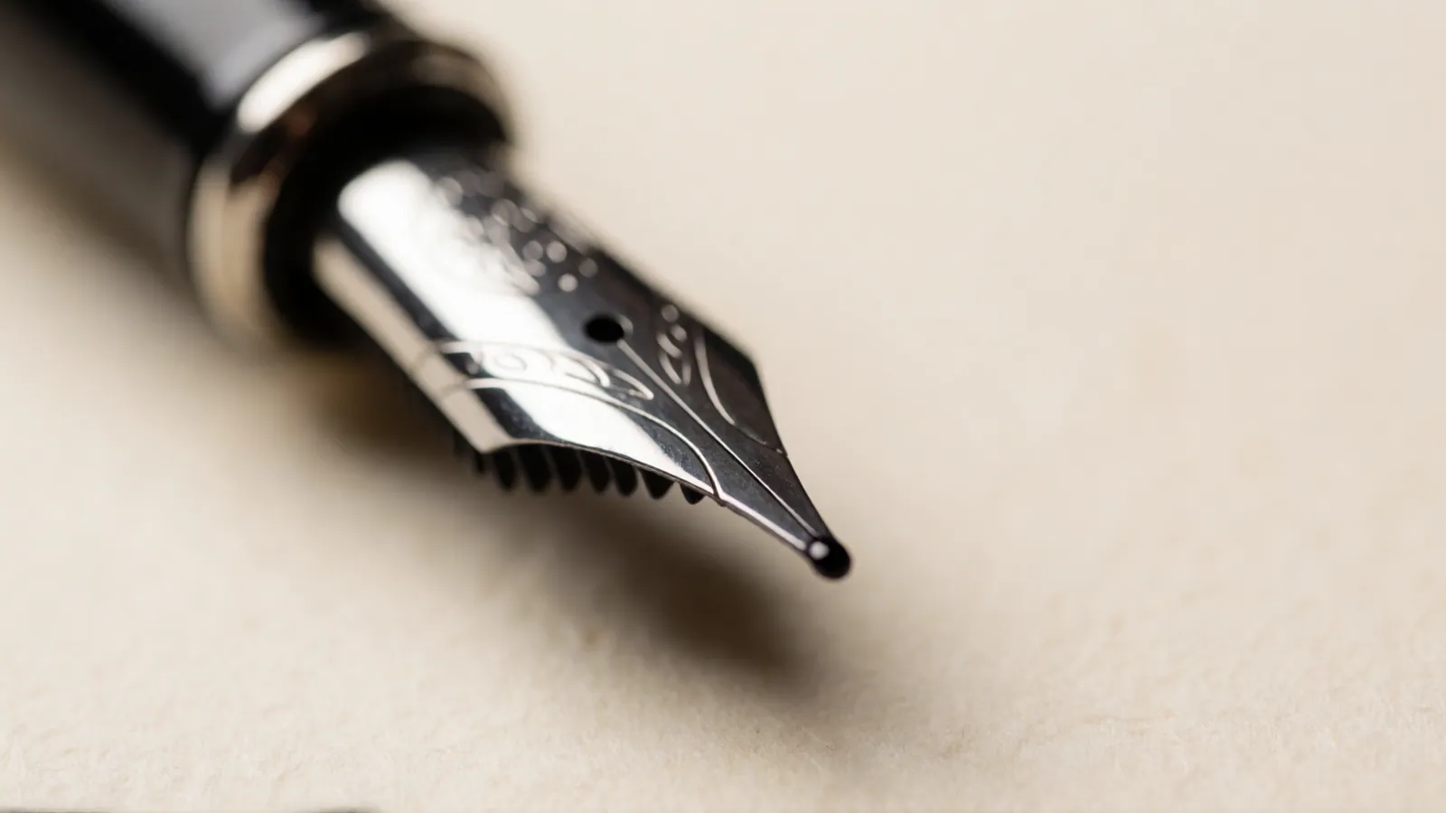A close view of blank paper, a pen nib and a bead of ink