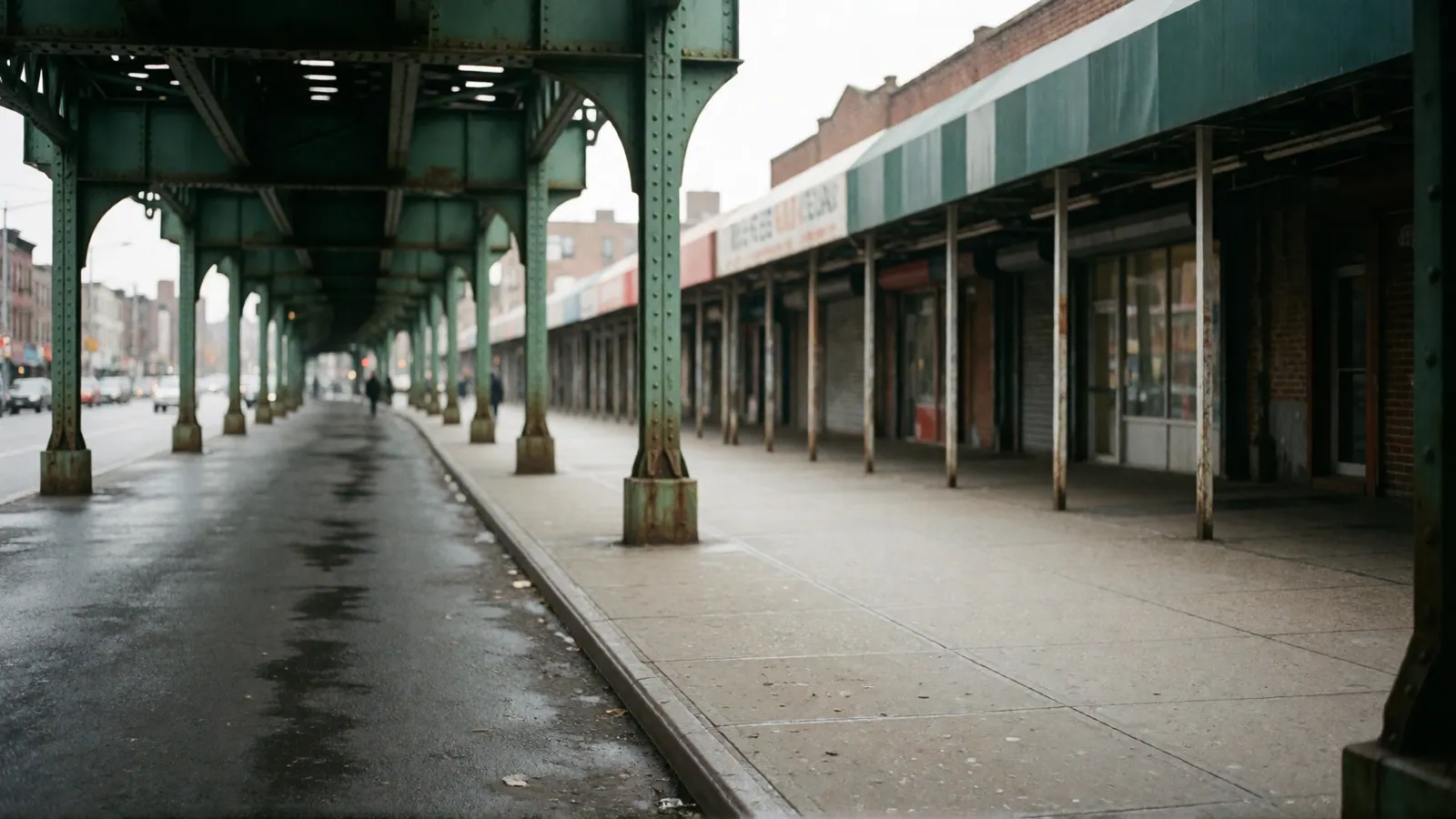 A pavement under an elevated railway in flat daylight, empty in both directions